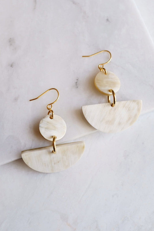 Pair of gold and beige half-circle earrings on a marble surface