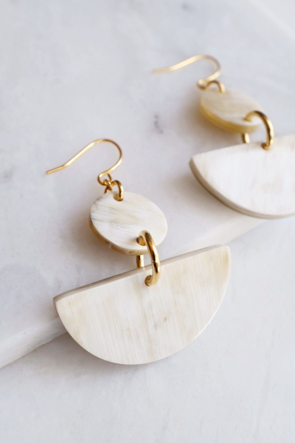 Pair of gold and bone half-circle earrings on a marble surface