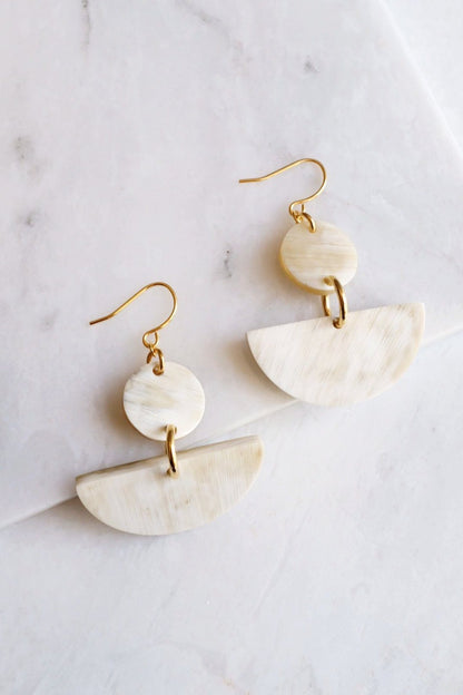 Pair of gold and beige half-circle earrings on a marble surface