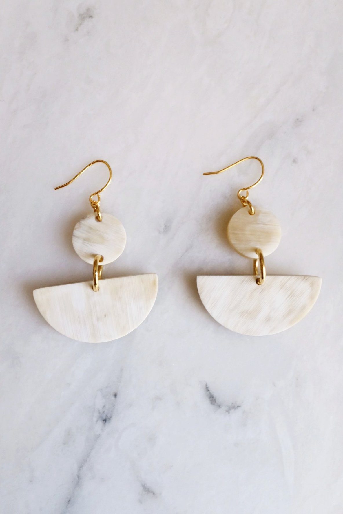 Pair of gold and beige earrings on a marble surface