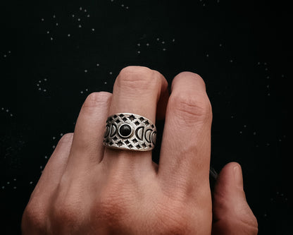 Hand wearing a silver ring with a black gemstone against a dark background