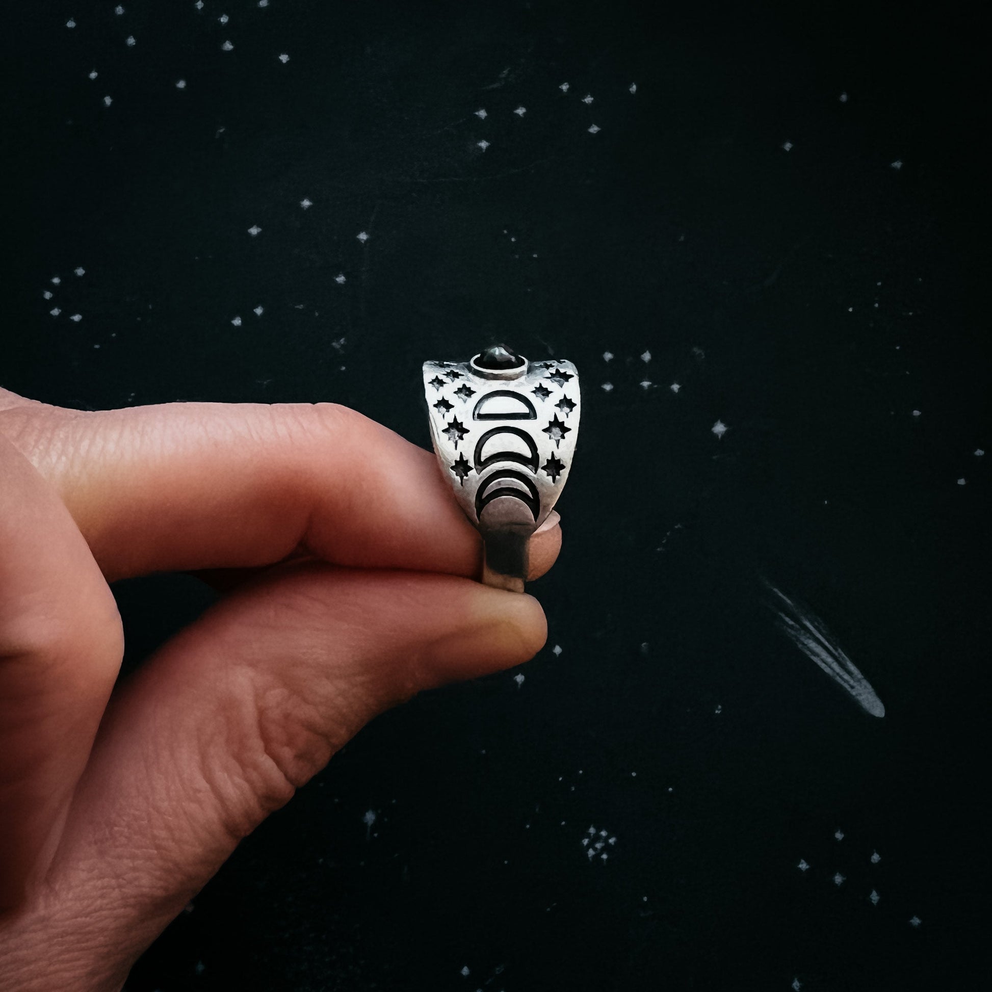 Hand holding a silver ring with star and moon design against a dark background