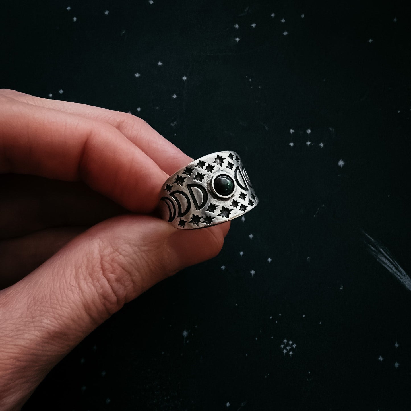 Silver ring with star patterns held by a hand against a dark background