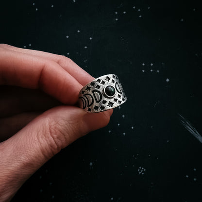 Silver ring with star patterns held by a hand against a dark background