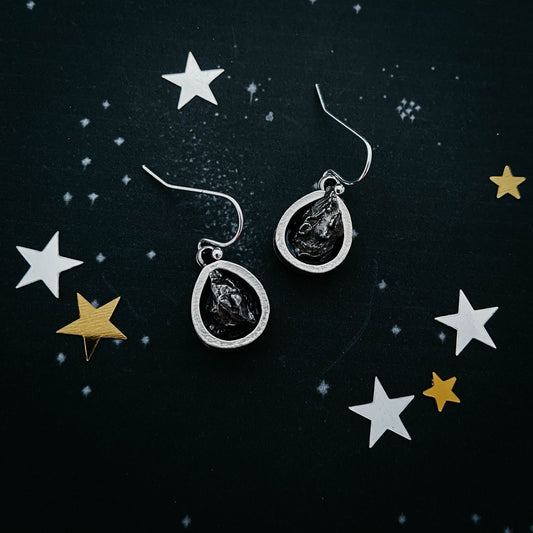 Silver earrings with black stones on a dark background with star decorations
