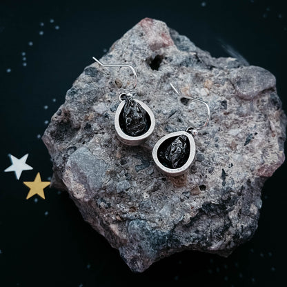 Silver earrings with black stones on a textured rock surface with star decorations.