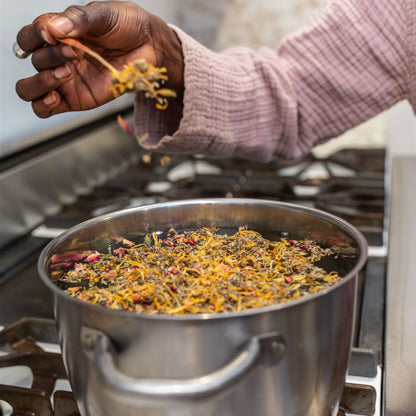 Person adding dried herbs to a pot on a stove