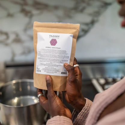 Person holding a package of Paavani Ayurvedic Herbal Ton Steam in a kitchen setting.