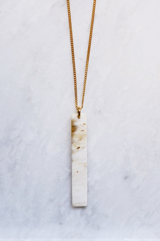 Necklace with a vertical, textured pendant on a marble surface