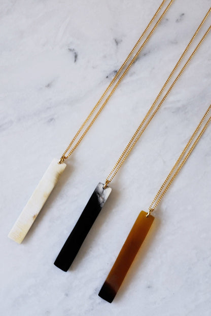 Three necklaces with different colored pendants on a marble surface