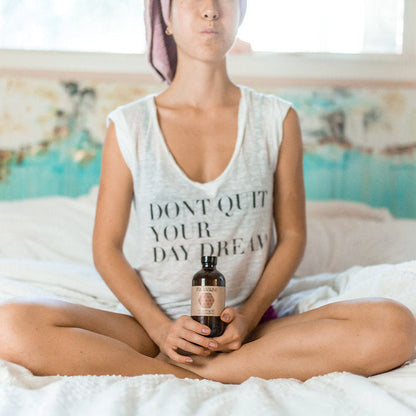 Person sitting on a bed holding a bottle with a visible brand label.