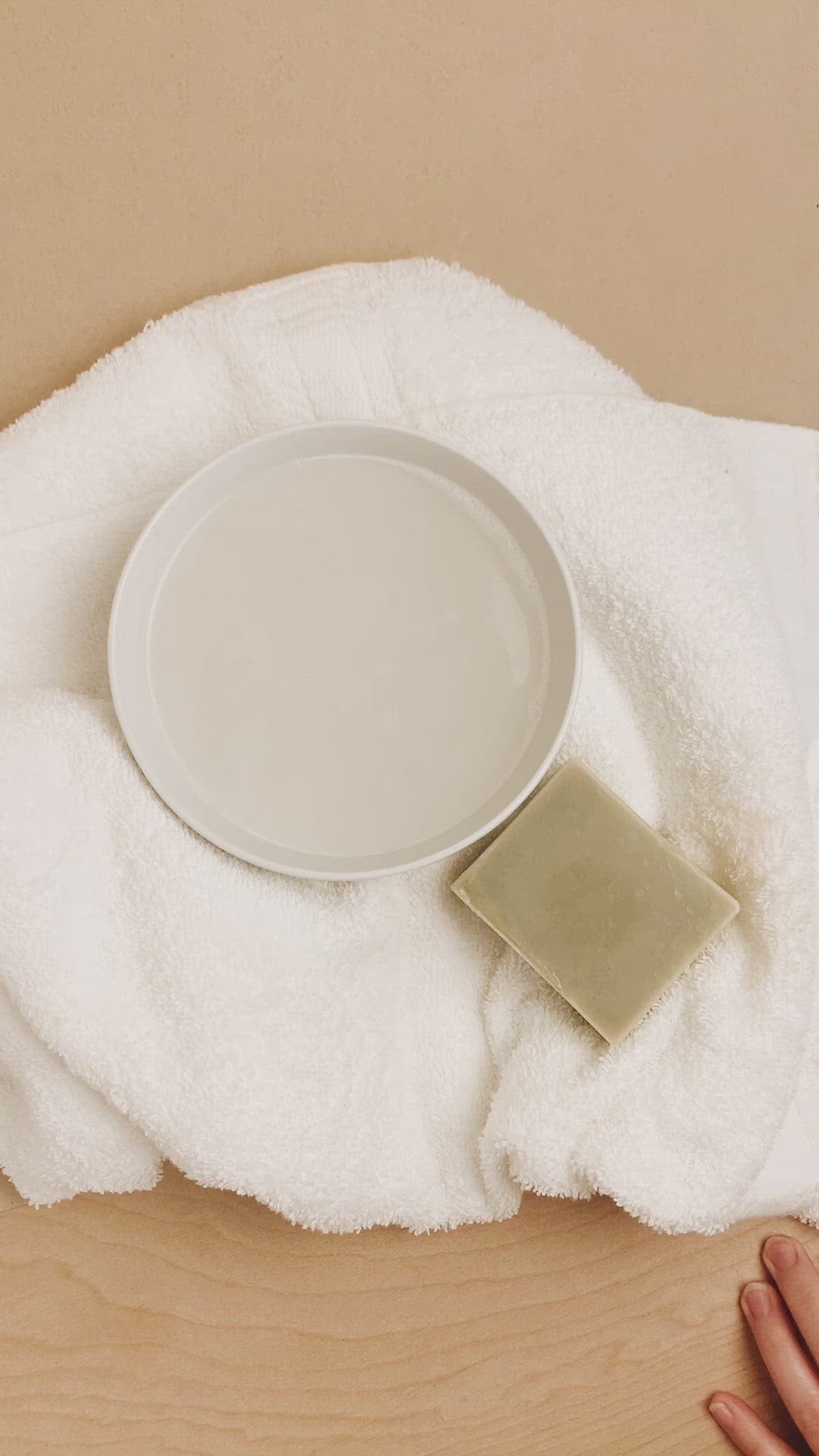 White ceramic bowl and bar of soap on a white towel with a beige background