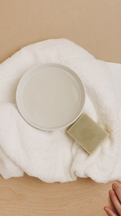 White ceramic bowl and bar of soap on a white towel with a beige background