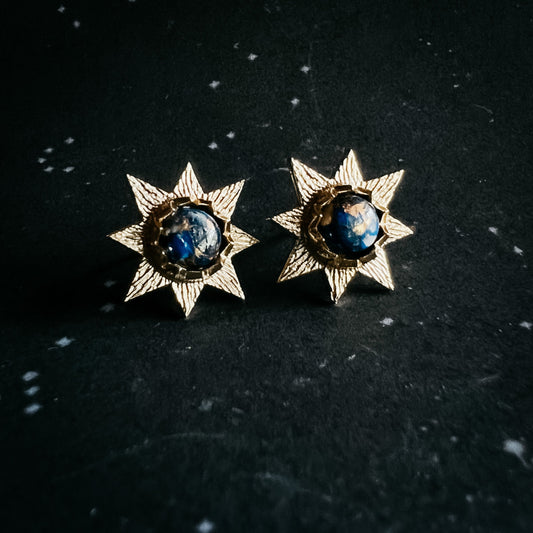 Pair of star-shaped earrings with blue gemstones on a dark background