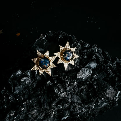 Star-shaped earrings with blue gemstones on a dark textured surface
