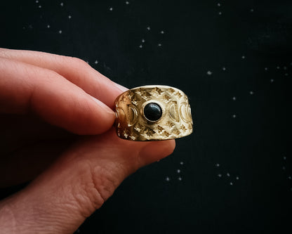 Gold ring with a black gemstone held by a hand against a dark background