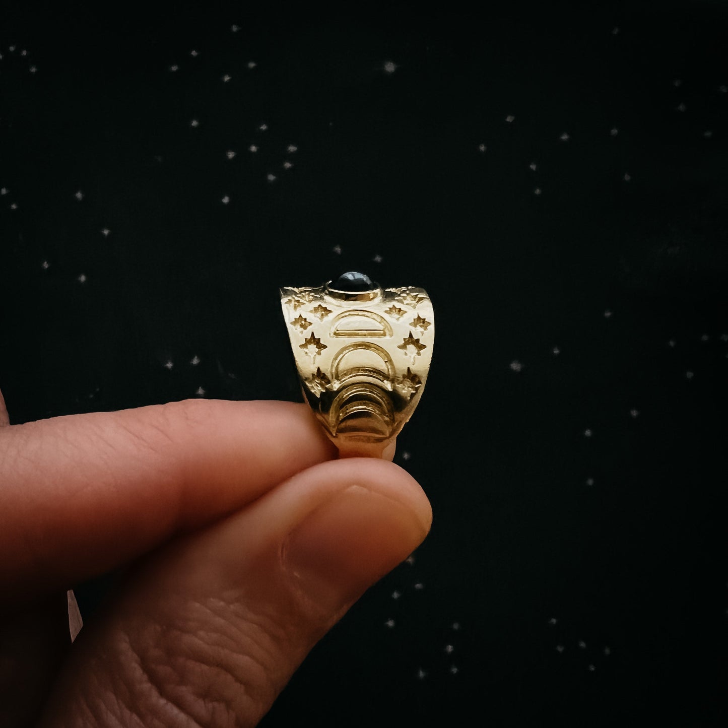 Gold ring with intricate design held between fingers against a black background