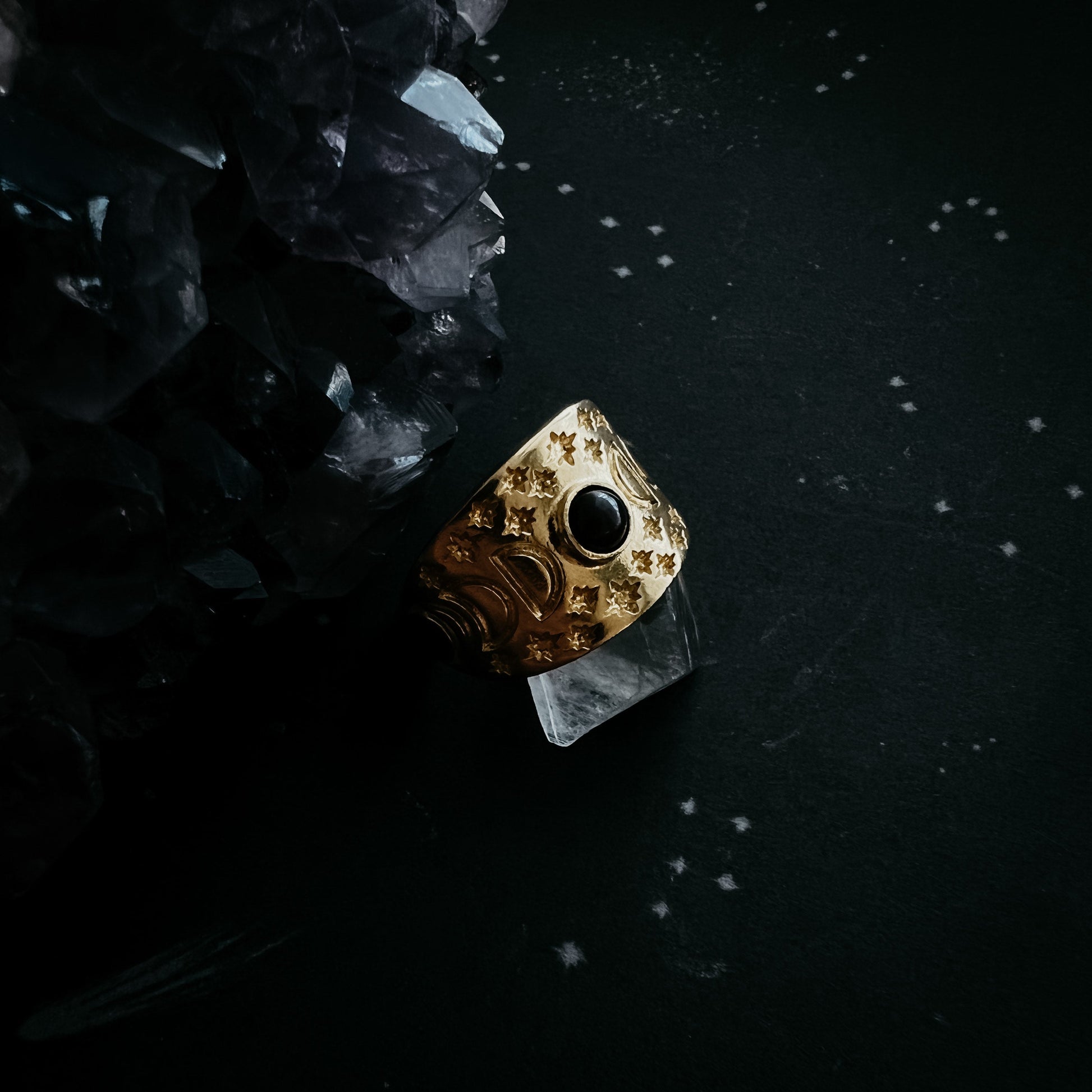 Gold ring with a black gemstone on a dark surface with crystals