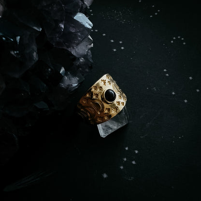 Gold ring with a black gemstone on a dark surface with crystals