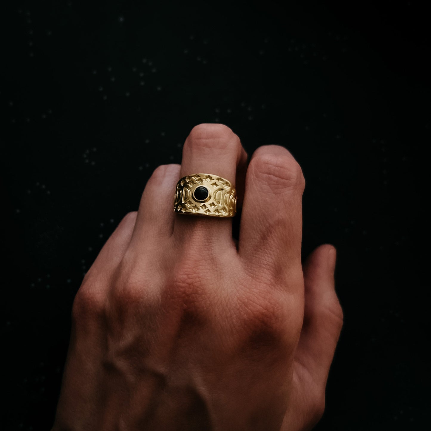 Gold ring with a black gemstone on a finger against a dark background
