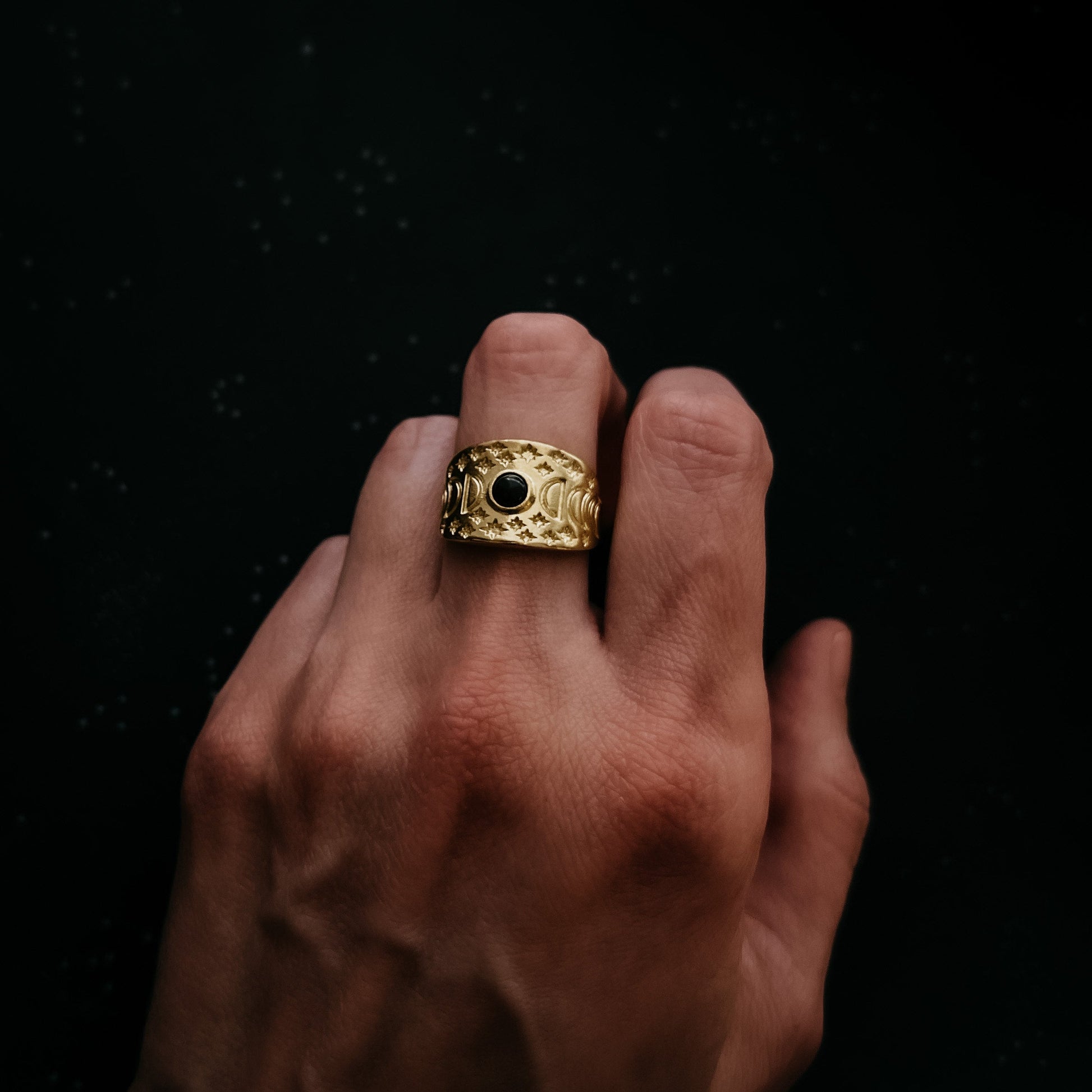 Gold ring with a black gemstone on a finger against a dark background