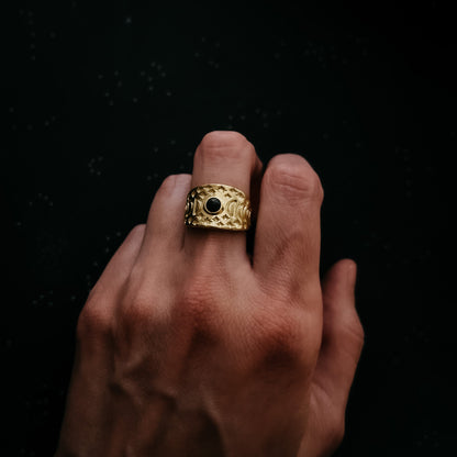Gold ring with a black gemstone on a finger against a dark background