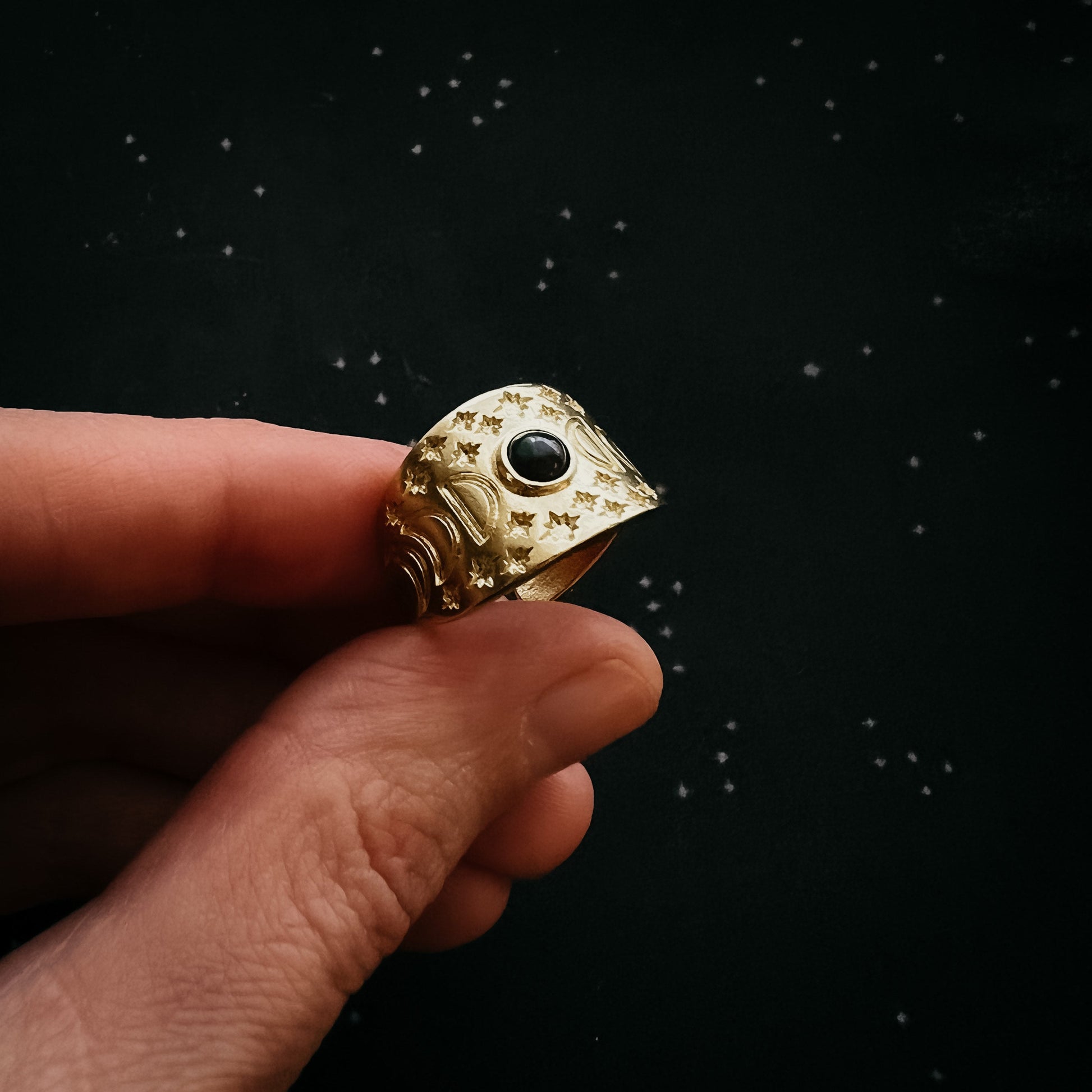 Gold ring with a black gemstone held between fingers against a dark background
