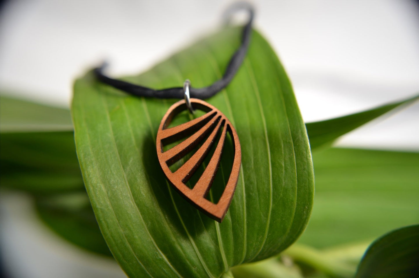 Copper leaf-shaped pendant on a black cord, resting on a green leaf with a blurred natural background.