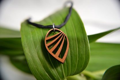 Copper leaf-shaped pendant on a black cord, resting on a green leaf with a blurred natural background.