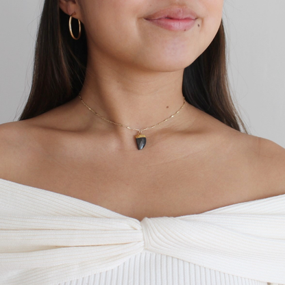 Woman wearing a delicate necklace with a black pendant on a plain background