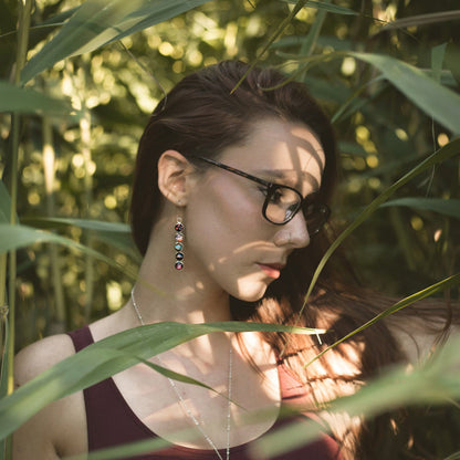 Woman with glasses and earrings standing among green plants