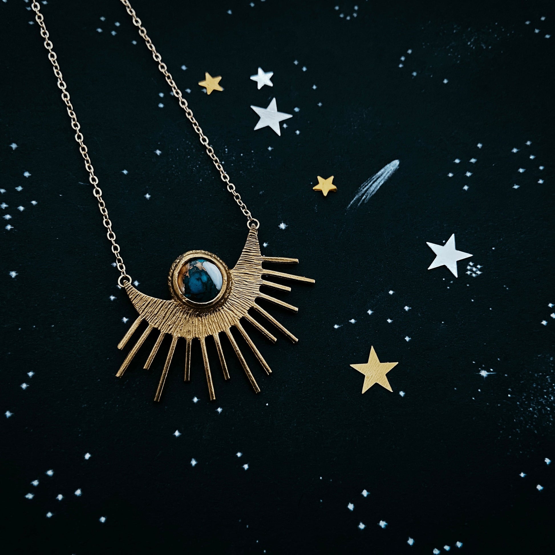Gold necklace with a sun-shaped pendant on a dark background with star illustrations