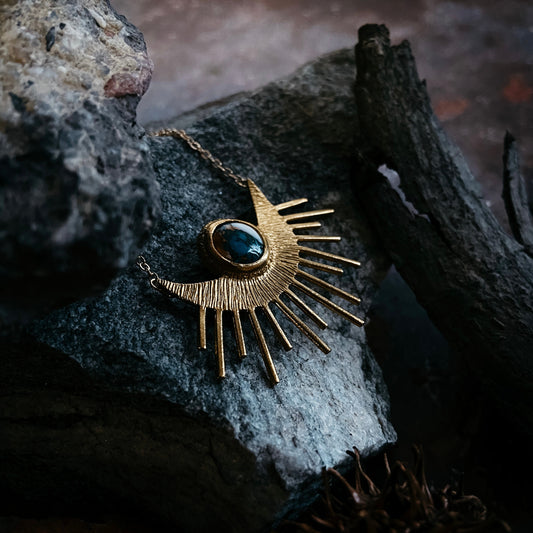 Gold necklace with a blue stone pendant on a textured rock surface