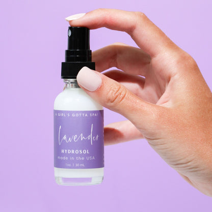 Hand holding a bottle of lavender hydrosol with a purple background
