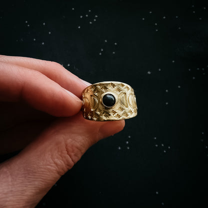 Gold ring with a black gemstone held by a hand against a dark background