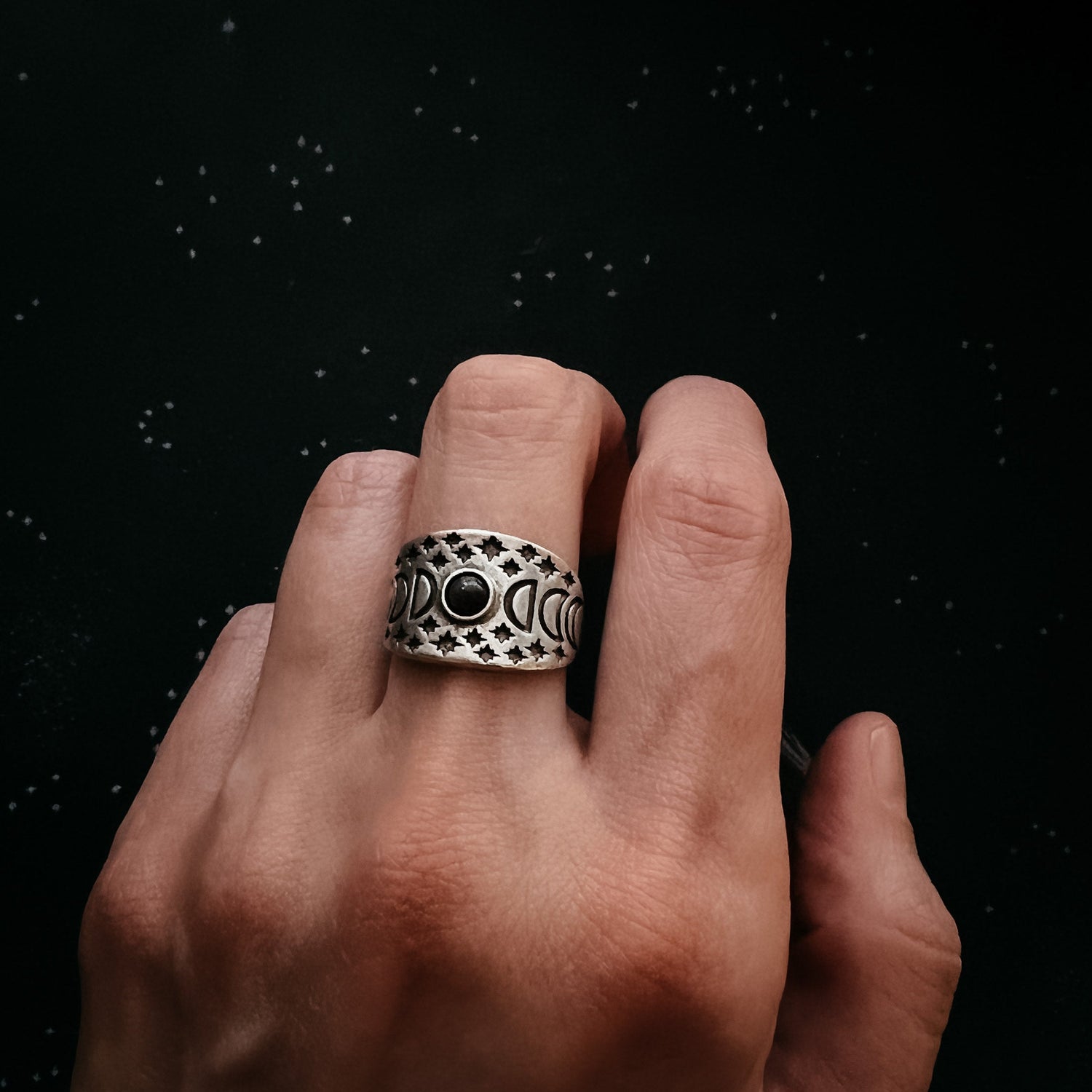 Hand wearing a silver ring with a black gemstone against a dark background
