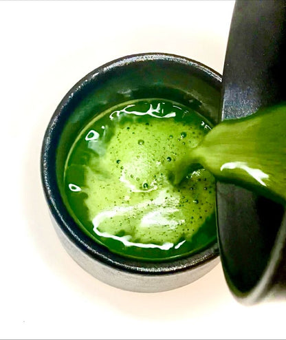 Green liquid being poured into a black cup on a white background