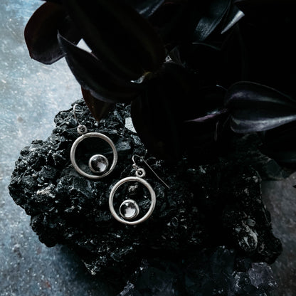 Silver circular earrings on a dark stone surface with leaves