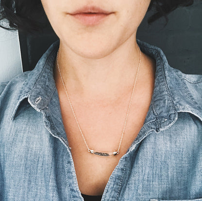 Person wearing a gold necklace with a minimalistic design, wearing a denim shirt.