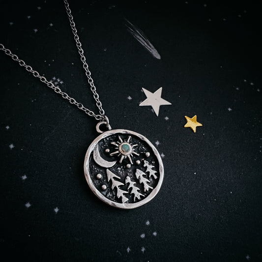 Silver necklace with a circular pendant featuring celestial designs on a dark background.