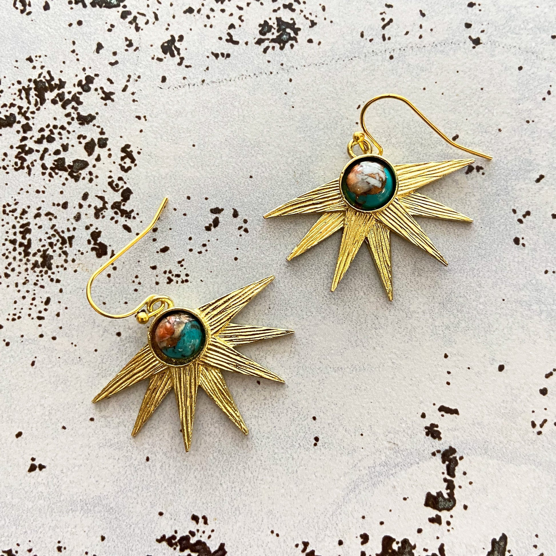 Gold sun-shaped earrings with gemstones on a textured surface
