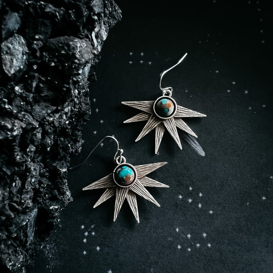 Star-shaped earrings with turquoise stones on a dark textured background