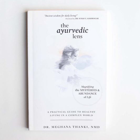 Book titled 'the ayurvedic lens' on a light gray background